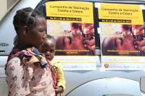 A woman and her baby walk past cholera vaccination campaign posters on the first day of the cho ...