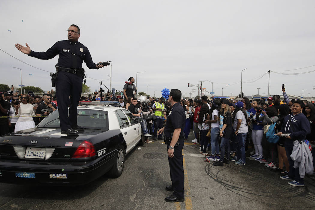 Los Angeles police officers tell the crowd to back up to clear the way for a hearse carrying th ...