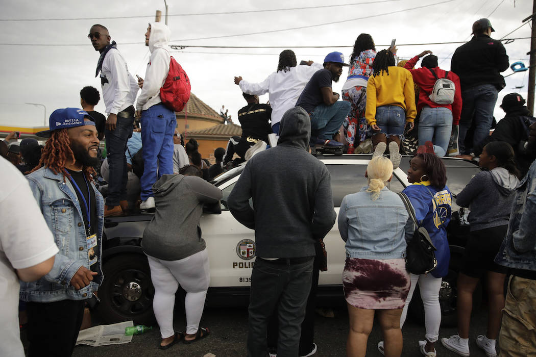 People climb on a police vehicle to watch a hearse carrying the casket of slain rapper Nipsey H ...