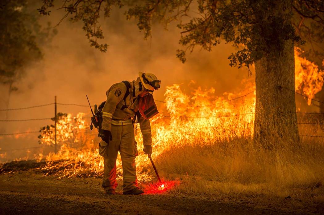 In this July 28, 2018, photo, a Cal Fire firefighter creates a back burn on Cloverdale Road nea ...