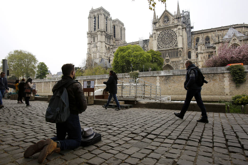 A man kneels as people came to watch and photograph the Notre Dame cathedral after the fire in ...