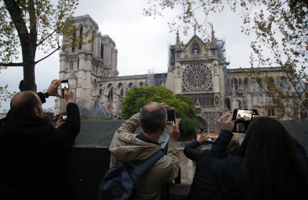 People take photos of the Notre Dame Cathedral in Paris, Tuesday April 16, 2019. Firefighters d ...