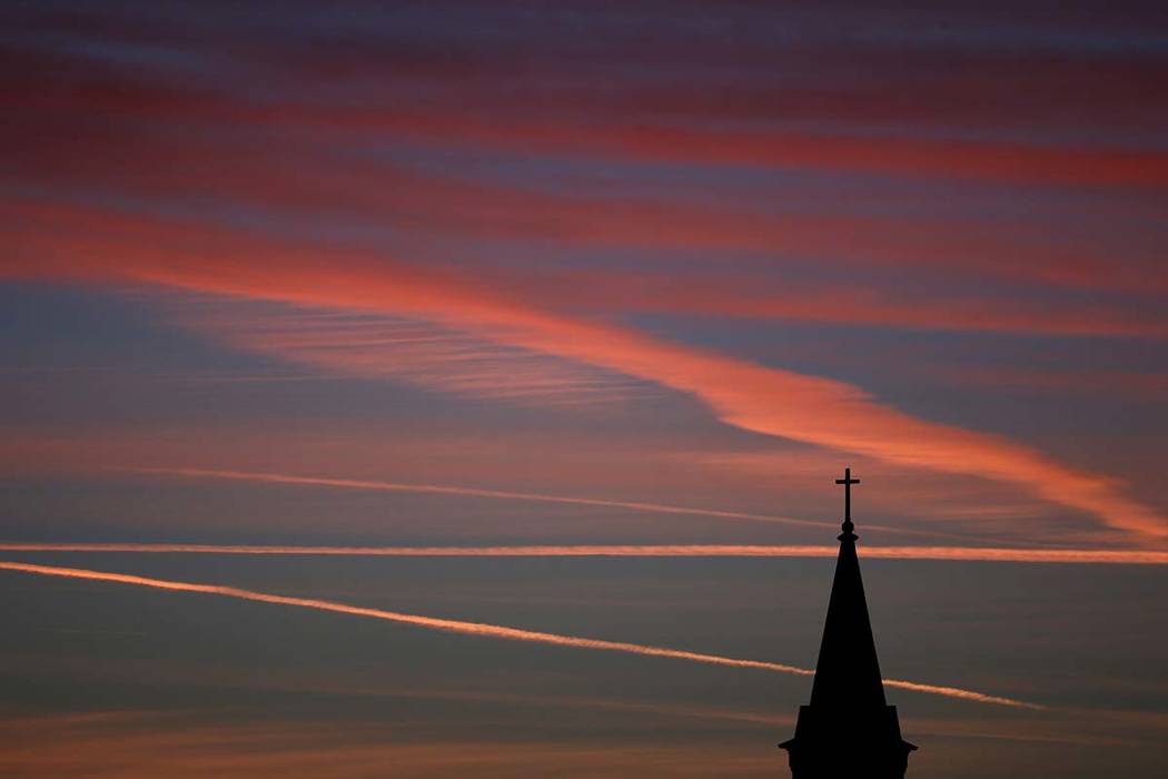 Contrails from jets glow pink as they are illuminated by the setting sun in the skies beyond a ...
