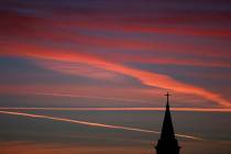 Contrails from jets glow pink as they are illuminated by the setting sun in the skies beyond a ...