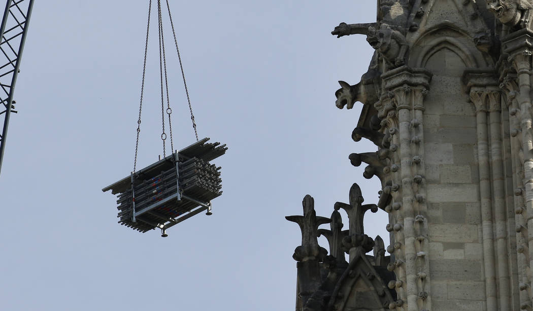 A crane hoists scaffolding past gargoyles outside the Notre Dame Cathedral in Paris, Thursday, ...
