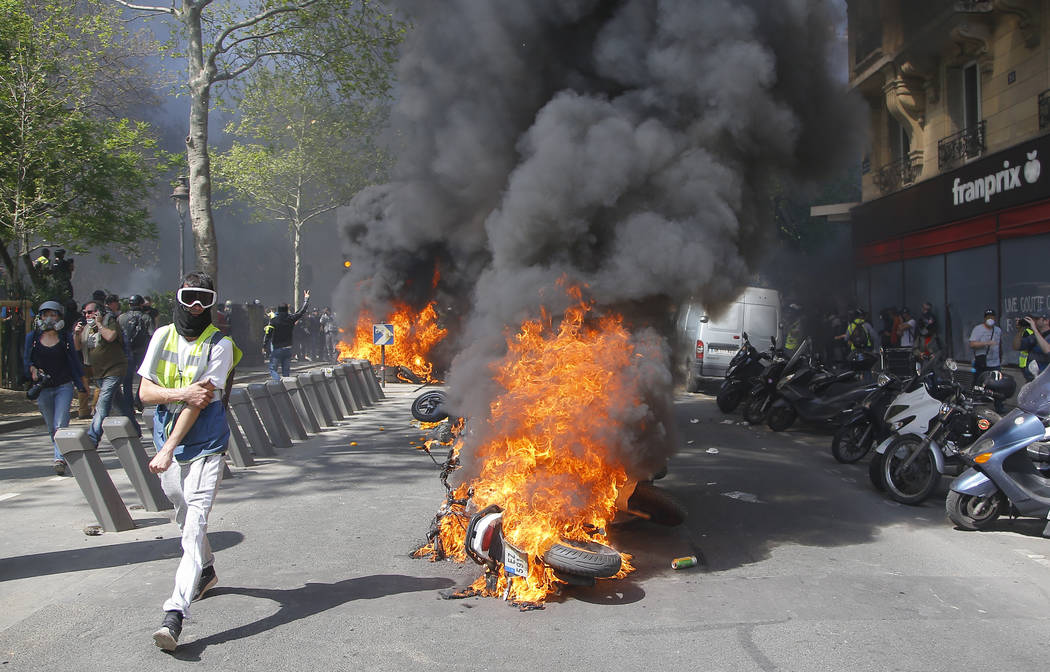 A man runs by a burning motorbike during a yellow vest demonstration in Paris, Saturday, April ...