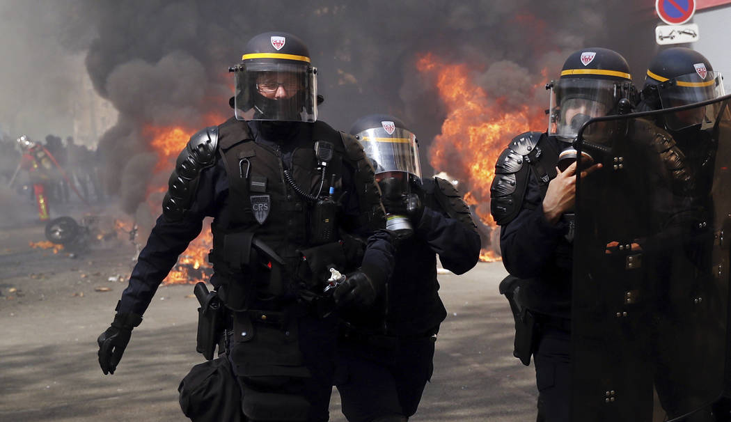 Police walk among burning vehicles during a yellow vest demonstration in Paris, Saturday, April ...