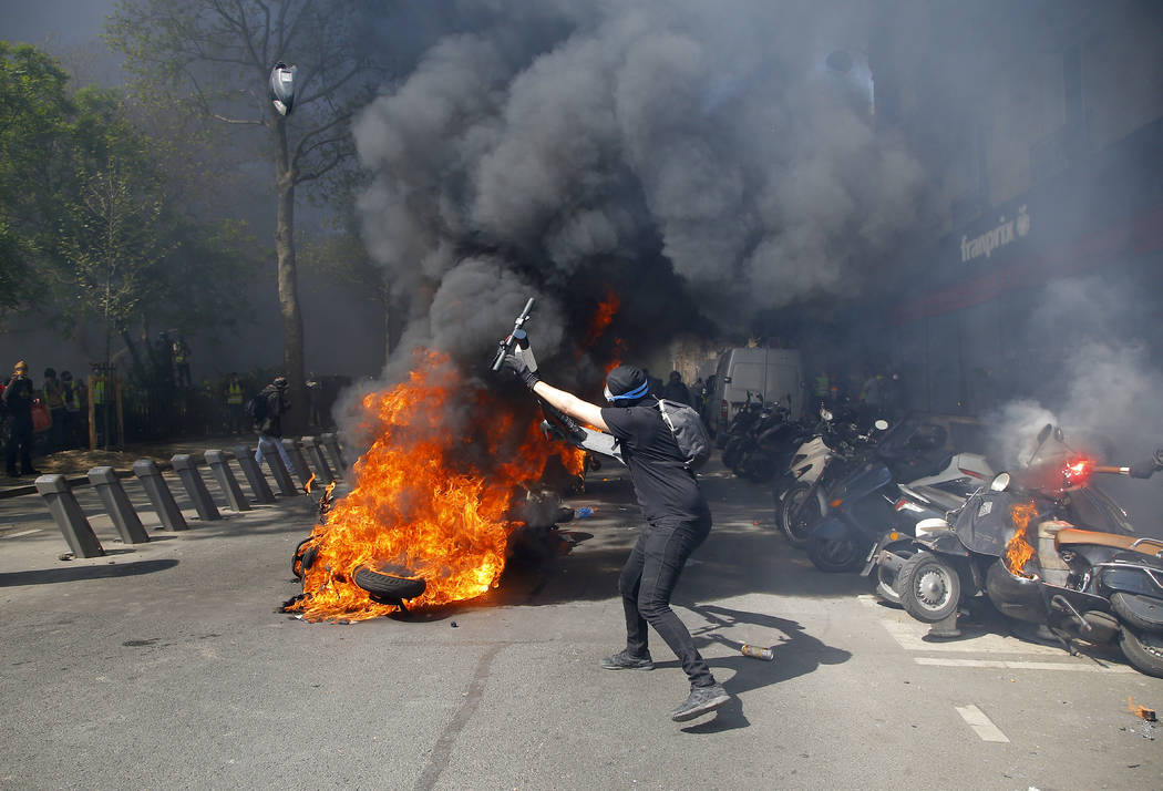 A protestor throws a scooter onto a pile of burning motorbikes during a yellow vest demonstrati ...