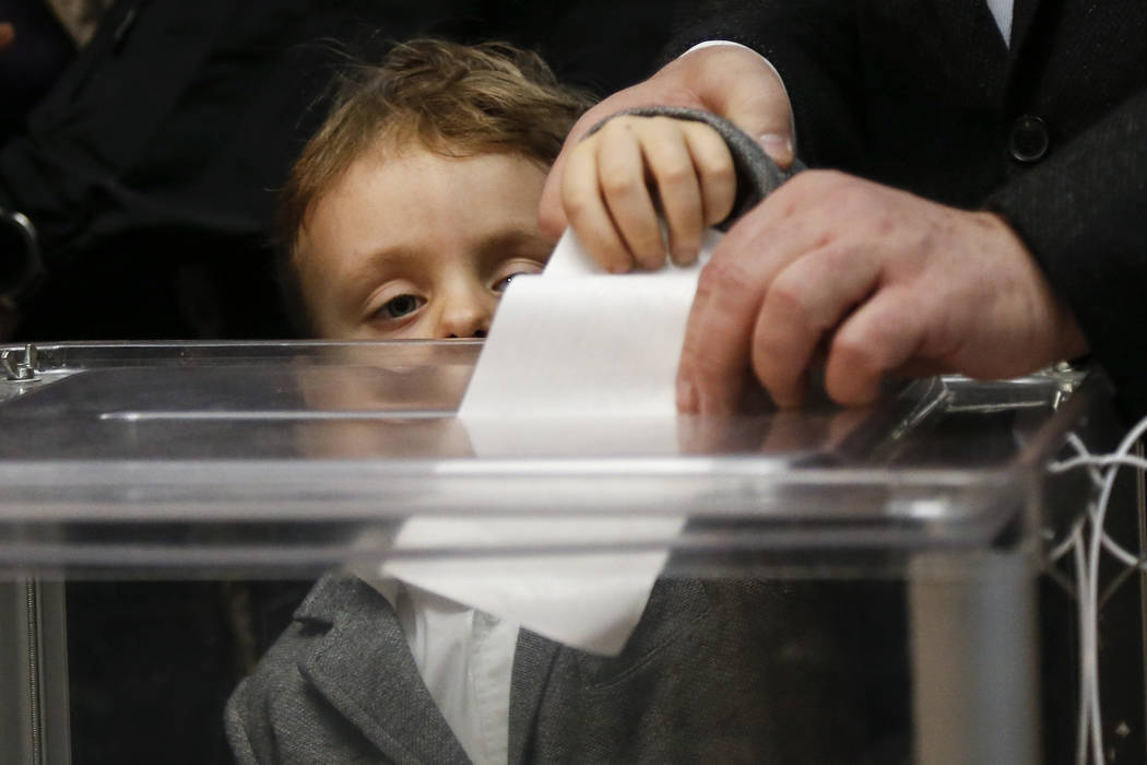 Ukrainian President Petro Poroshenko casts his ballot as his grandson Petro, looks at the ballo ...