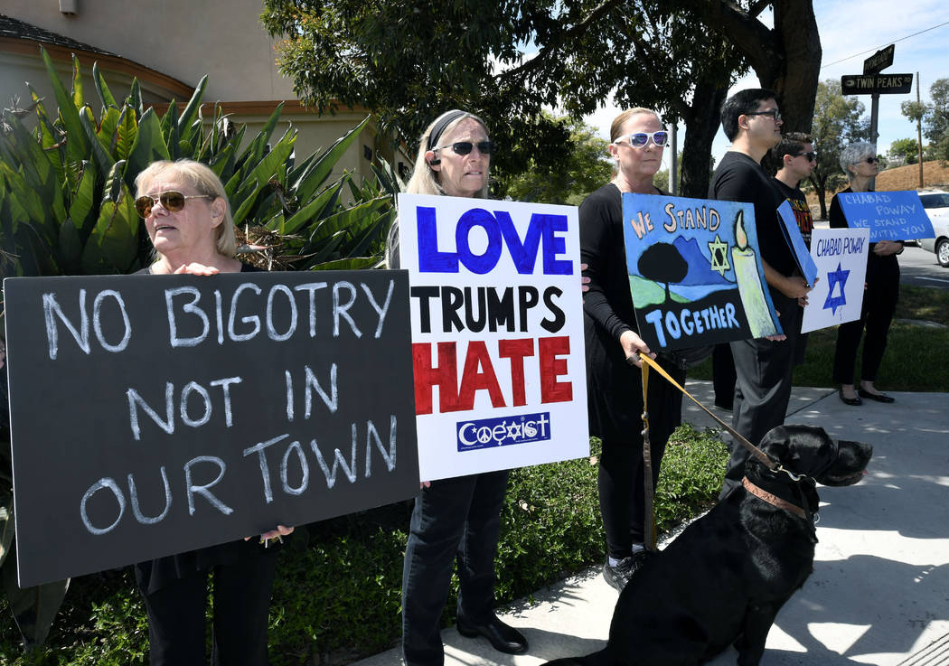 People gathering on a street corner hold signs in support of the victims of the Chabad of Poway ...