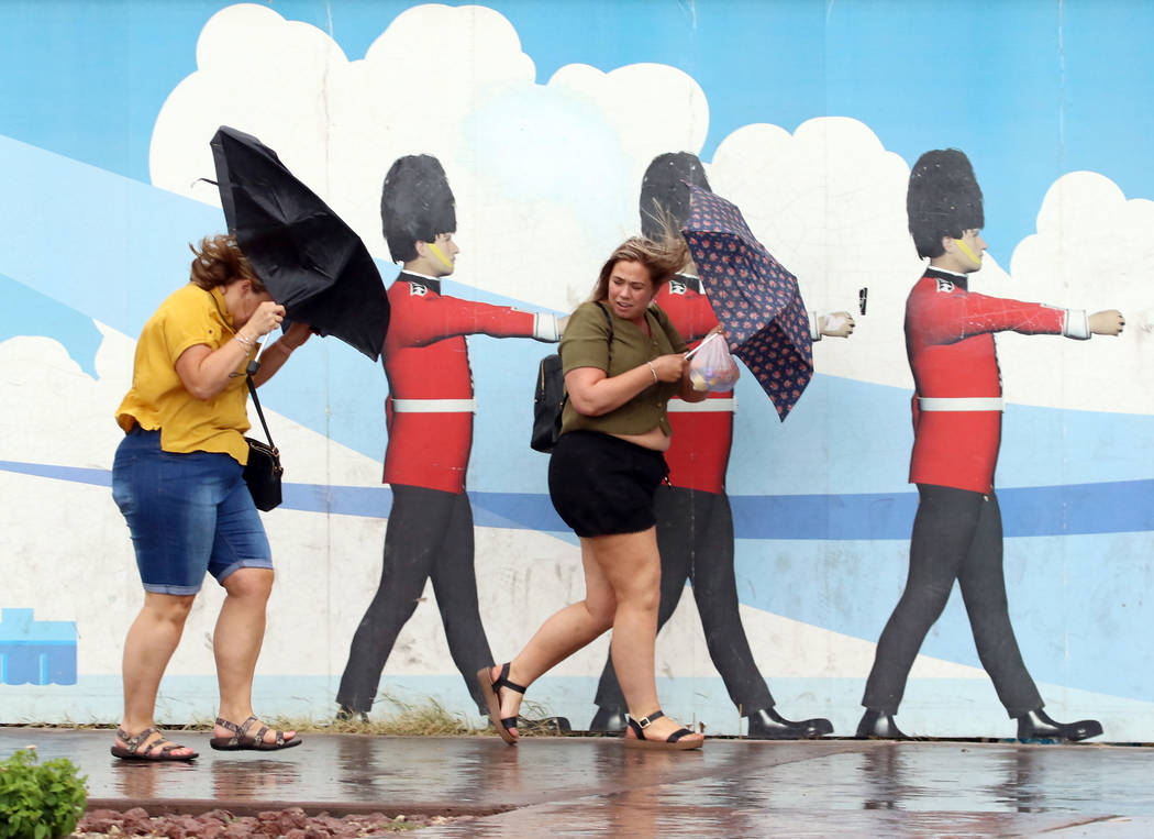 Pedestrians hold umbrellas to protect themselves from heavy winds and rain as they walk along L ...