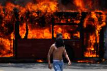 An anti-government protester walks near a bus that was set on fire by opponents of Venezuela's ...