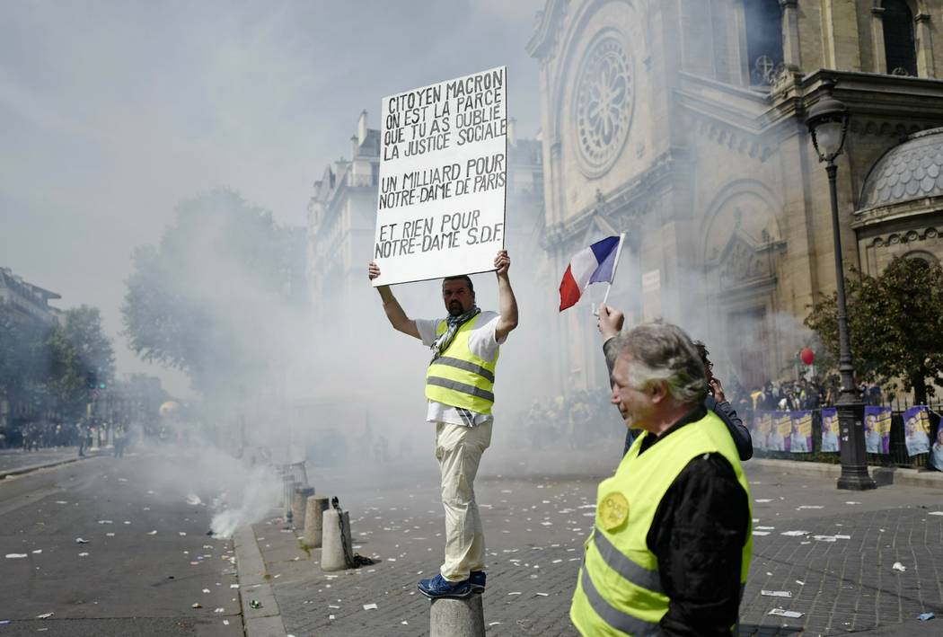 A protestor holds a banner criticising the funding of the Notre Dame cathedral renovations, dur ...