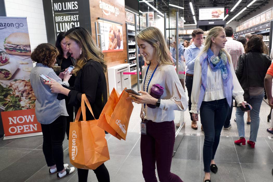 Customers walk out of a newly-opened Amazon Go store with their shopping bags, Tuesday, May 7, ...