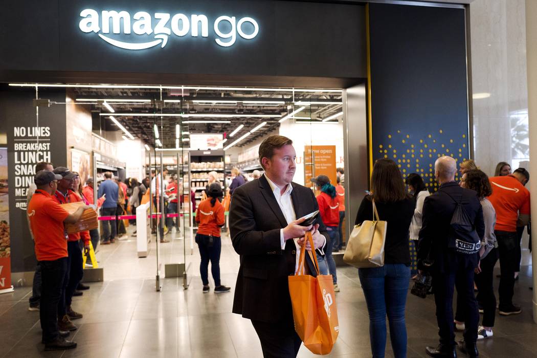 A customer carries his shopping bag as she walks out of a newly-opened Amazon Go store, Tuesday ...