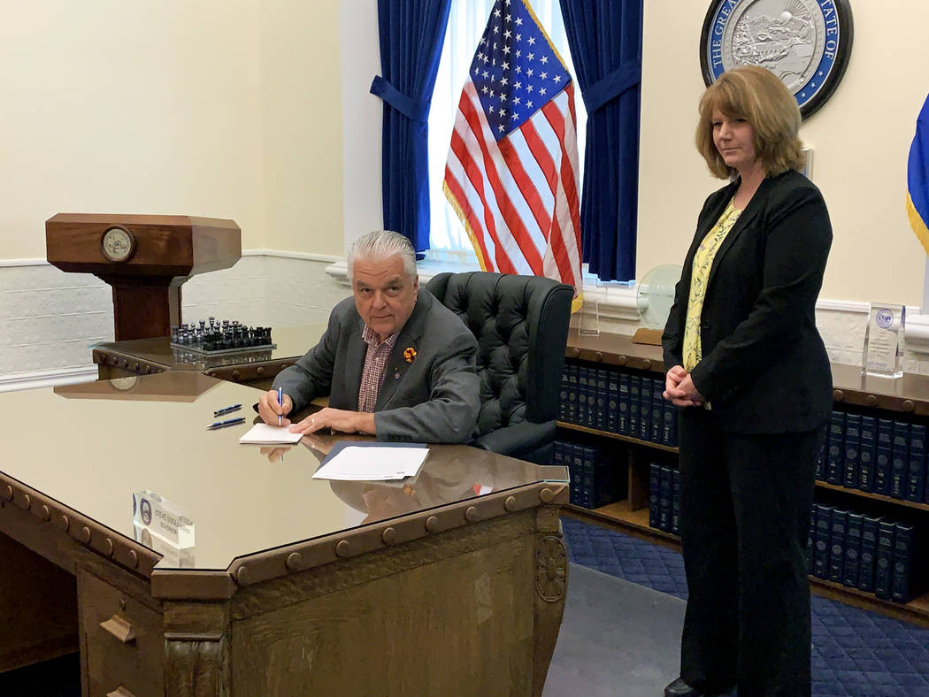 Gov. Steve Sisolak, left, checks the time as he signs Senate Bill 32, which increases transpare ...