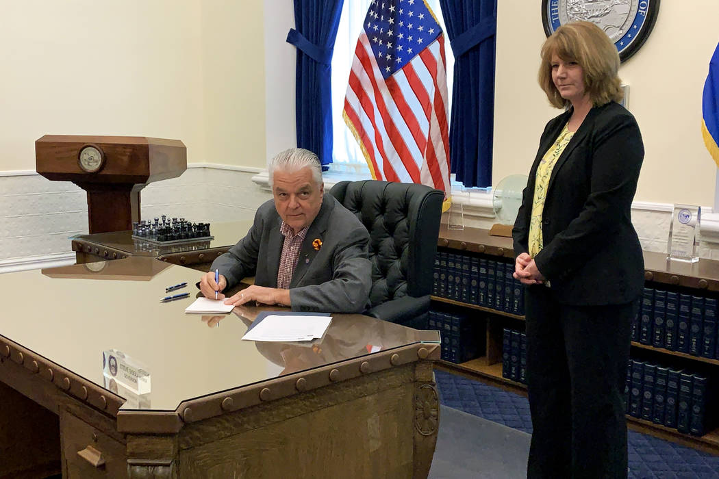 Gov. Steve Sisolak, left, checks the time as he signs Senate Bill 32, which increases transpare ...