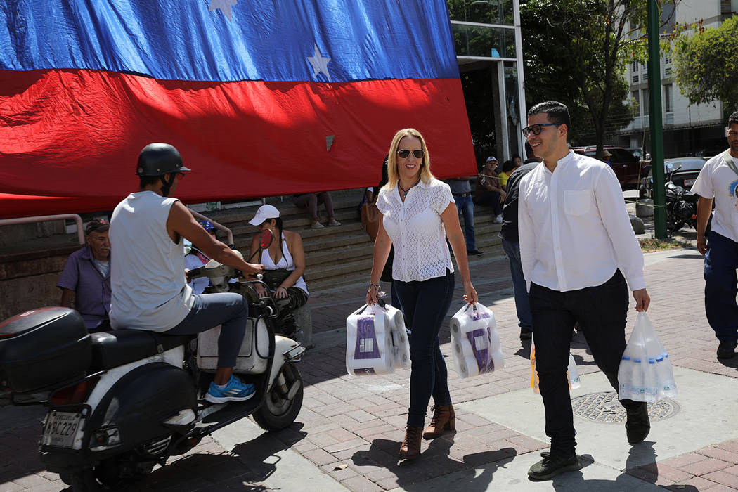 A couple, carrying their purchases of toilet paper and bottled water, walk through a plaza wher ...