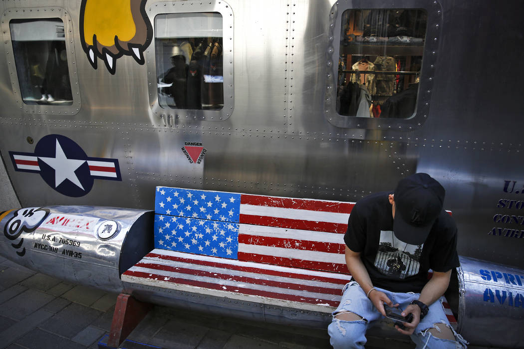A man browses his smartphone on a bench with a decorated with U.S. flag outside a fashion bouti ...