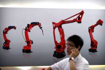 A visitor talks on his smartphone in front of a display of manufacturing robots from a Chinese ...