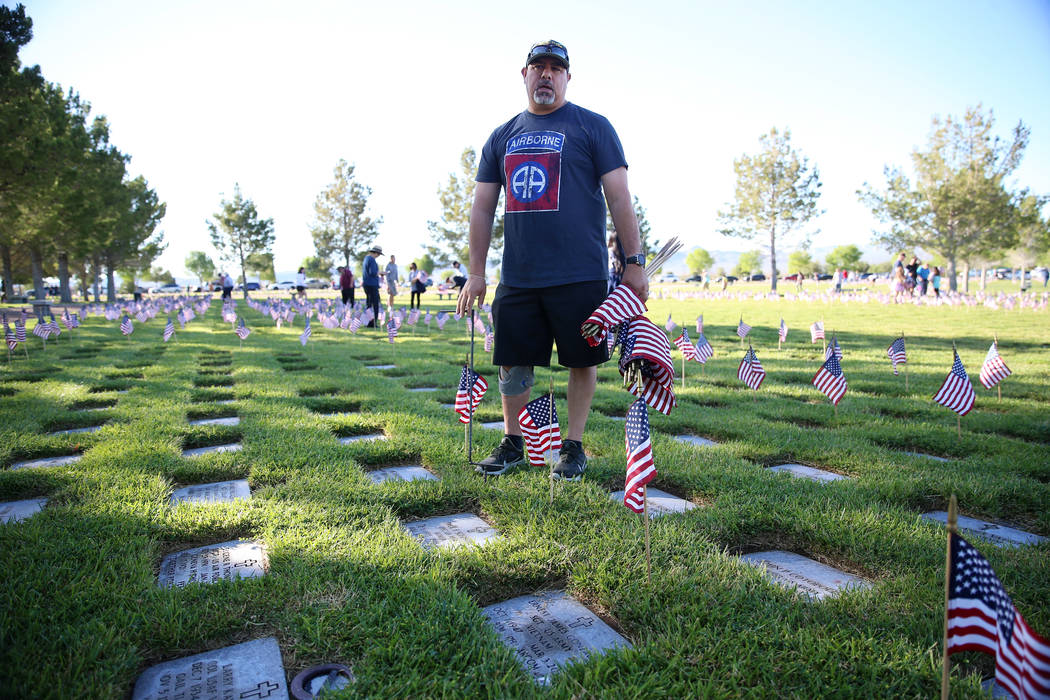 Volunteer Ernie Gonzales, U.S. Army veteran, assisting with placing American flags on gravesite ...