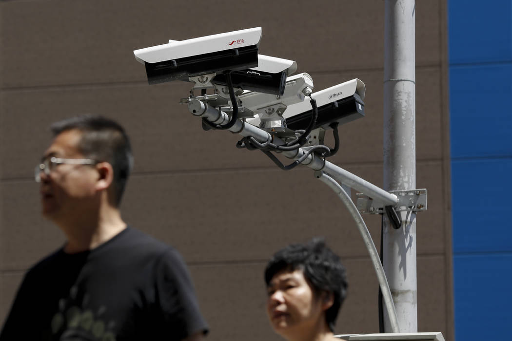 People walk by Chinese-made surveillance cameras installed along a street in Beijing, Thursday, ...