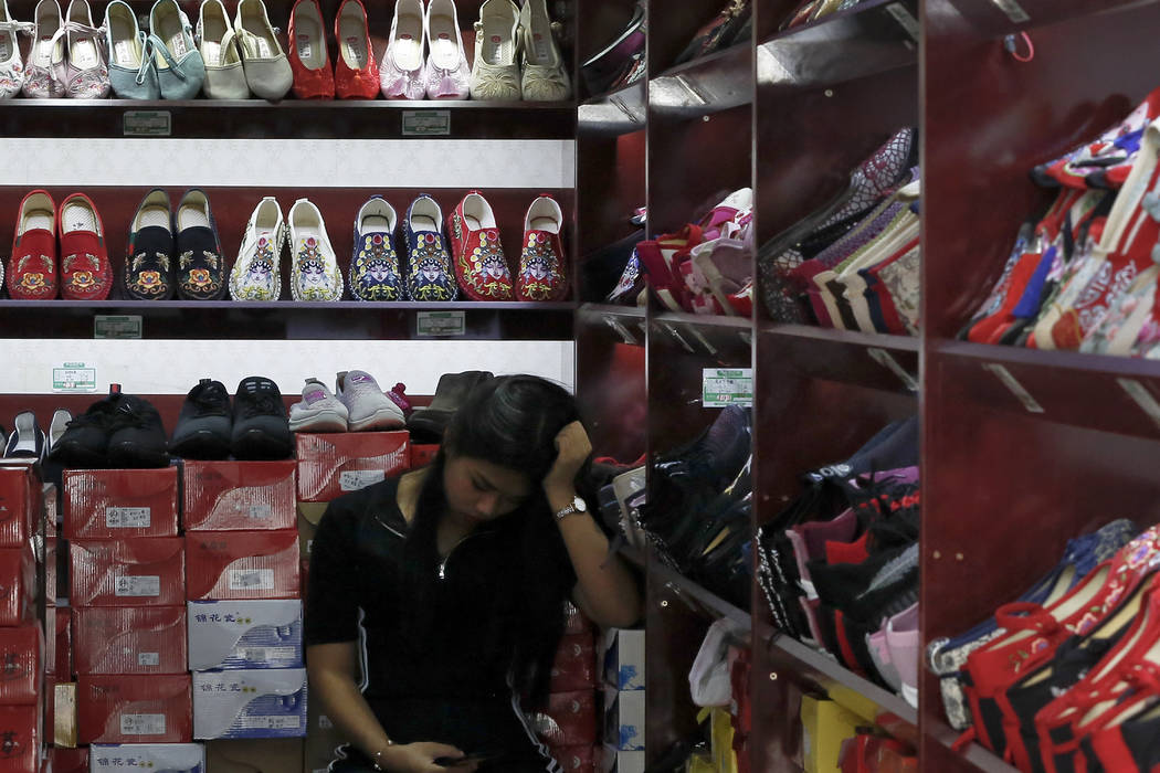 A worker browses her smartphone inside a shop selling shoes in Beijing, Thursday, May 23, 2019. ...