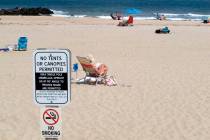 In this Monday, May 20, 2019 photo, beachgoers sit on the sand beyond a sign indicating that sm ...