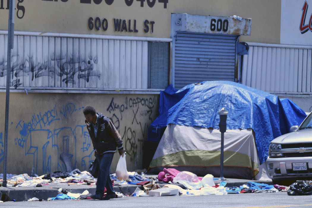 A homeless man walks along a street lined with trash across the street from LAPD Central Commun ...