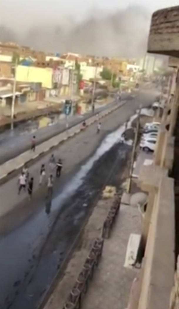 In this image made from video, civilians walk down a street in Khartoum, Sudan with plumes of s ...