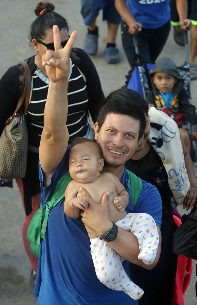 A migrant father carries his child as hundreds of Central American migrants walk on the highway ...
