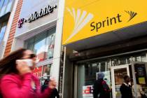In an April 27, 2010 file photo, a woman using a cell phone walks past T-Mobile and Sprint stor ...