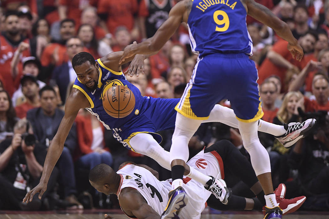 Golden State Warriors forward Kevin Durant, left, falls over Toronto Raptors center Serge Ibaka ...