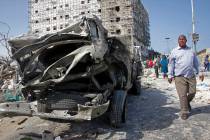 A man walks past the wreckage of an official vehicle that was destroyed in a bomb attack in the ...