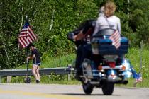 A motorcycle passes as a woman leaves flowers at the scene of a fatal accident on Route 2 in Ra ...