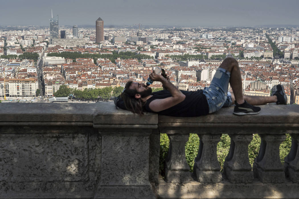 A man drinks as he cools off in the shade above Lyon, central France, Thursday, June 27, 2019. ...
