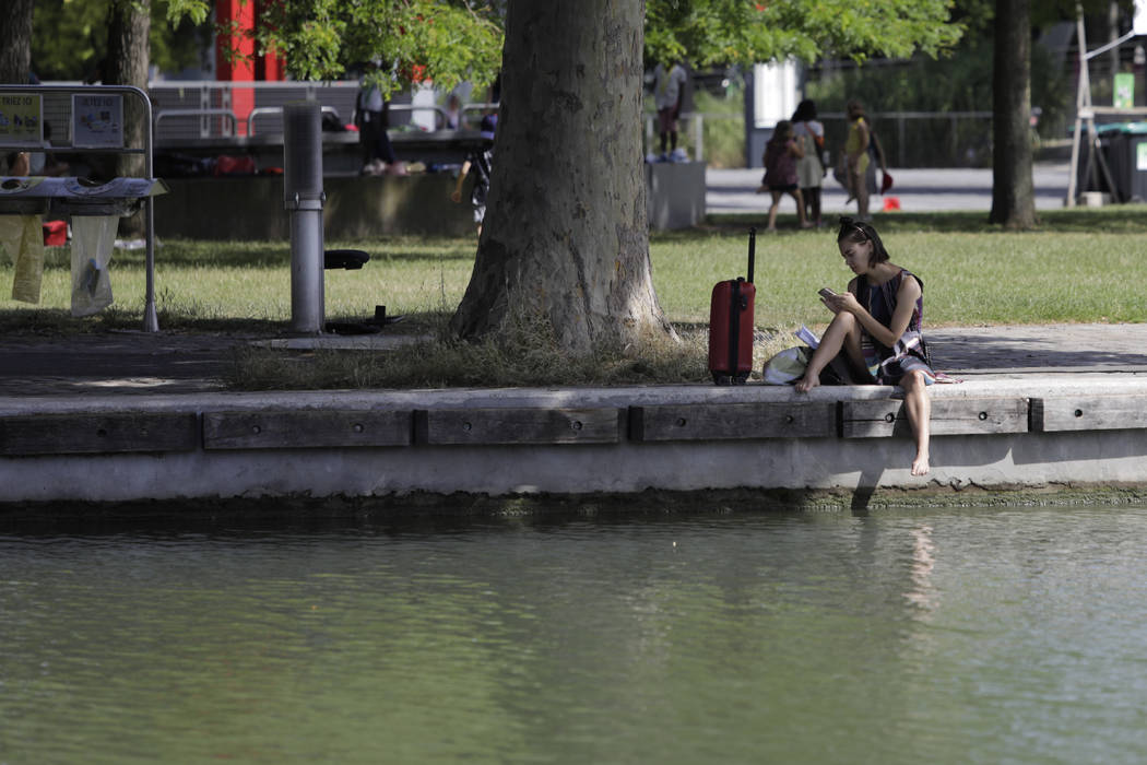 A woman sits in the shade along the Canal de l'Ourcq in Paris, Friday, June 28, 2019. Schools a ...