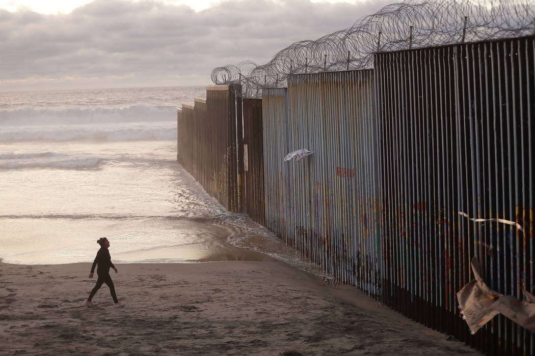 FILE - In this Jan. 9, 2019 file photo, a woman walks on the beach next to the border wall topp ...