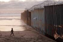 A woman walks on the beach next to the border wall topped with razor wire in Tijuana, Mexico, i ...