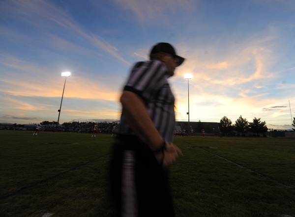 A football official runs across the field as the sun sets in the first quarter of a high sch ...