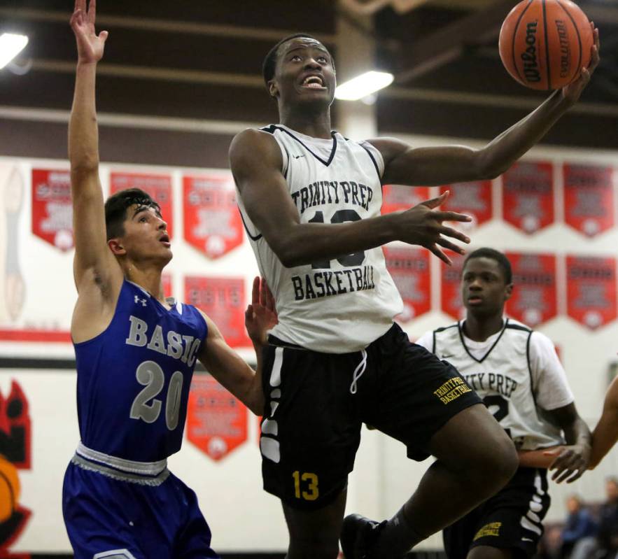 Trinity’s Zaba Bangala (13) jumps up to take a shot while under pressure from Basic&#8 ...