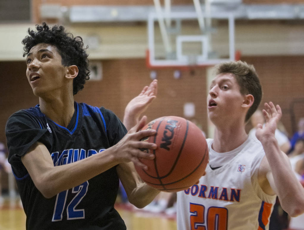Desert Pines freshman Milos Uzan (12) drives past Bishop Gorman senior guard Noah Taitz (20) ...