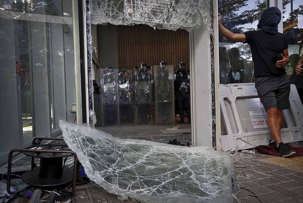 Police officers with shields stand guard behind the damaged glass of the Legislative Council af ...