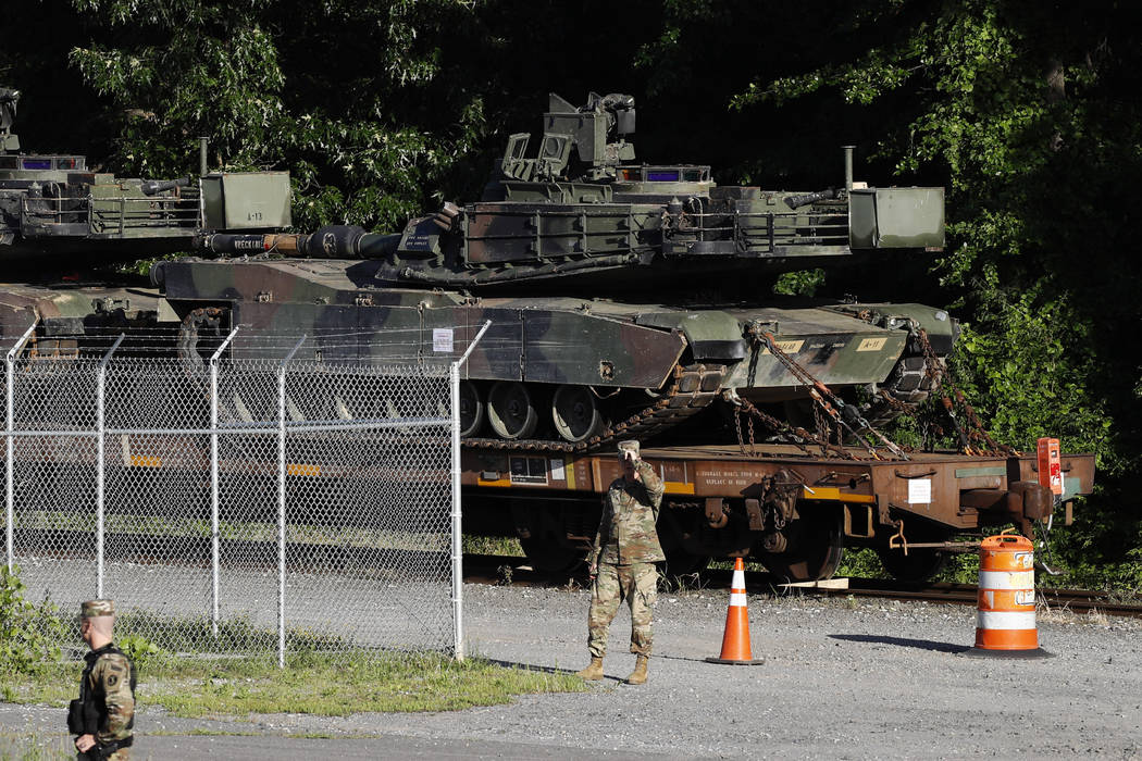 Military police walk near Abrams tanks on a flat car in a rail yard, Monday, July 1, 2019, in W ...