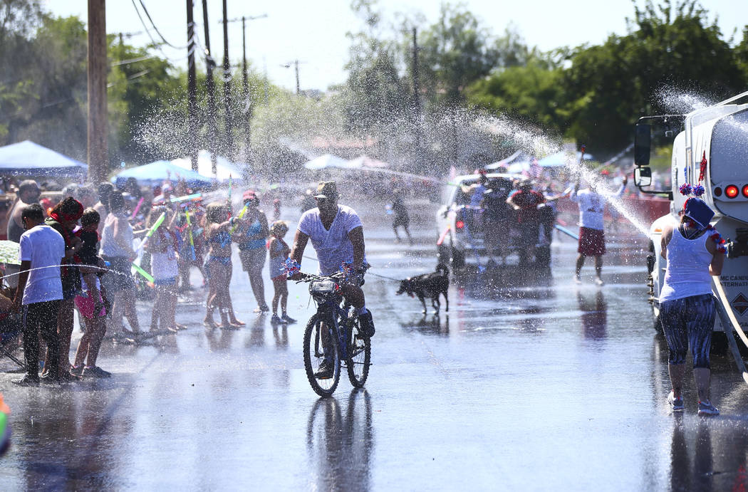 A man rides a bicycle as spectators and parade participants spray water during the parade at th ...