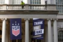 A worker hangs signs at City Hall one day ahead of a ticker-tape parade for the U.S. Women's Wo ...