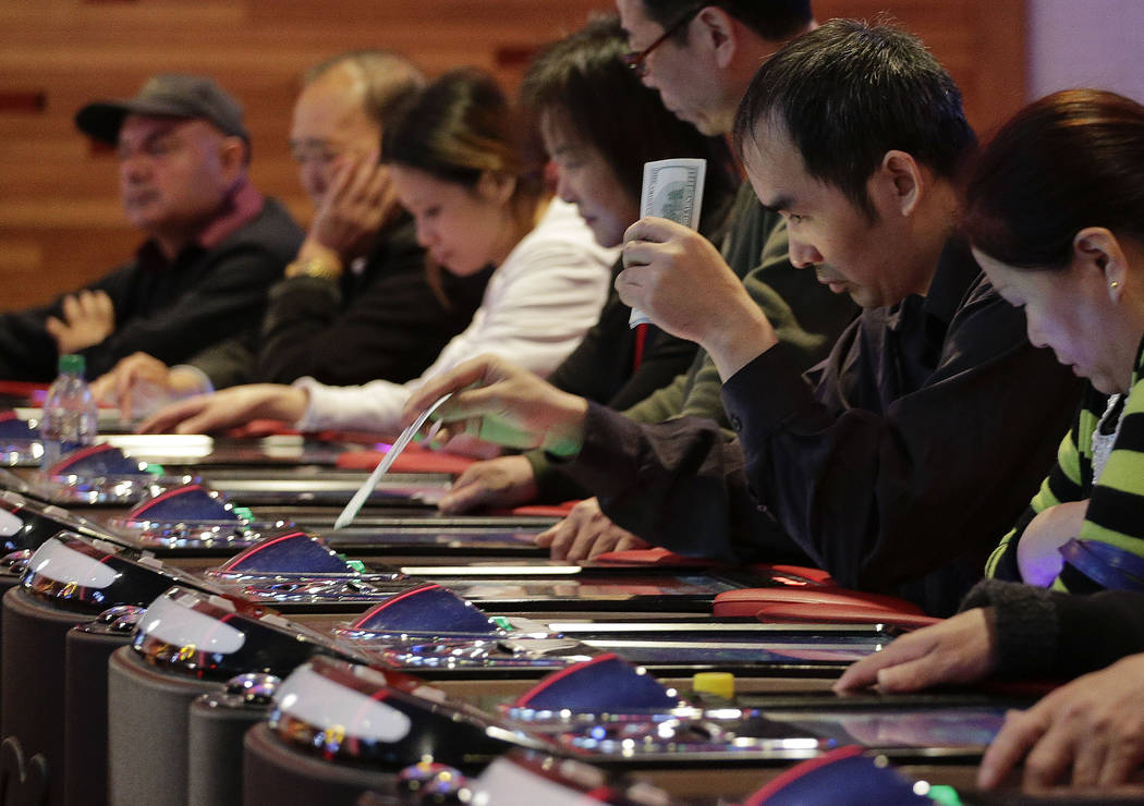 A gambler slides a $100 bill into an electronic baccarat game at the Resorts World Casino at th ...