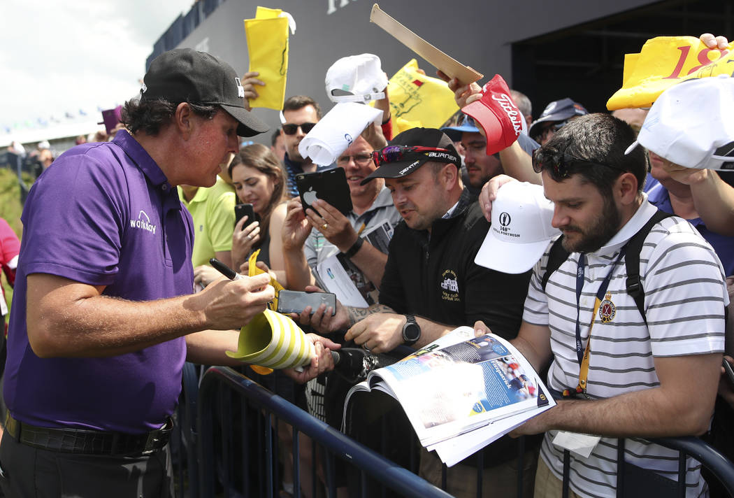 Phil Mickelson of the United States signs autographs on the 18th fairway during a practice roun ...