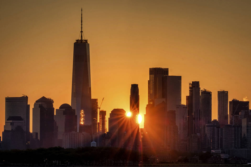 The sunlight flares around the buildings in lower Manhattan as the sun rises, Monday, July 1, 2 ...