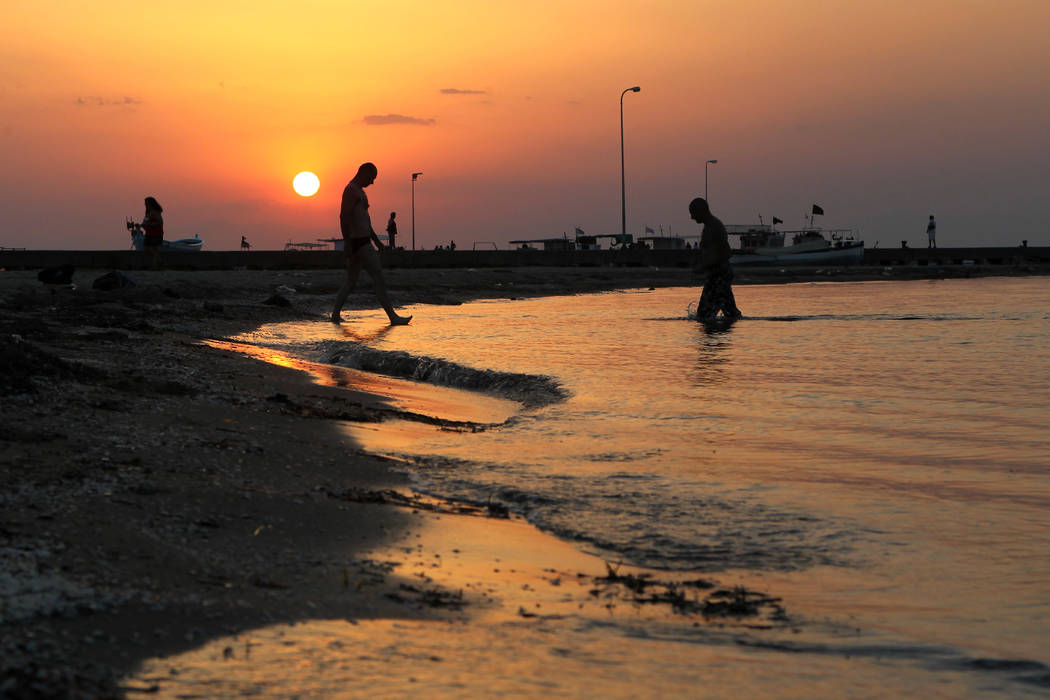 Bathers walk at the public beach of Perea during sunset, in the eastern suburbs of Thessaloniki ...